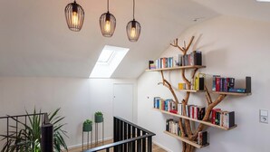 A modern interior with a wooden bookshelf shaped like a tree, a staircase with black railings, and hanging pendant lights. - Overlook Lodge - Exclusive 5-Star Vacation Home on Lake Eder in Kellerwald (Vöhl)