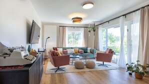 A modern living room with a sofa set, a coffee table, and a flat-screen TV mounted on the wall. - Overlook Lodge - Exclusive 5-Star Vacation Home on Lake Eder in Kellerwald (Vöhl)
