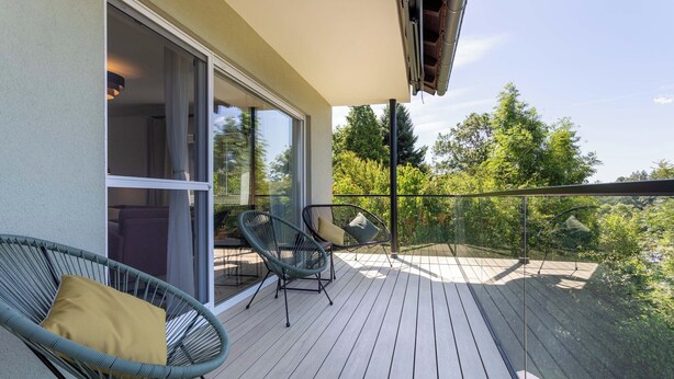 A balcony with wooden flooring, two green wicker chairs with cushions, and a glass door leading to an interior space. - Overlook Lodge - Exclusive 5-Star Vacation Home on Lake Eder in Kellerwald (Vöhl)