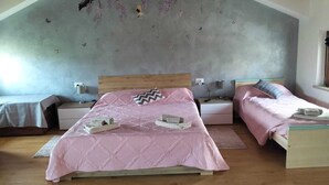 A bedroom with a sloped ceiling, a large bed with a pink quilted bedspread, two bedside tables with lamps, and a window with a view of the sky.