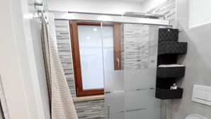 A modern bathroom with a glass shower enclosure, a toilet, and a small sink.