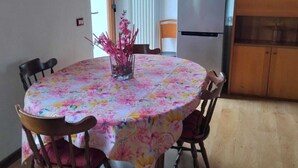 A dining area with a round table covered in a floral tablecloth, surrounded by wooden chairs.