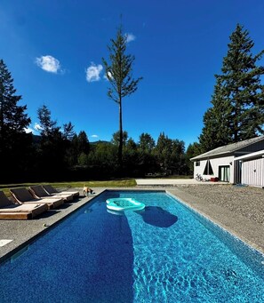 A swimming pool with lounge chairs, a floating ring, and a building in the background.