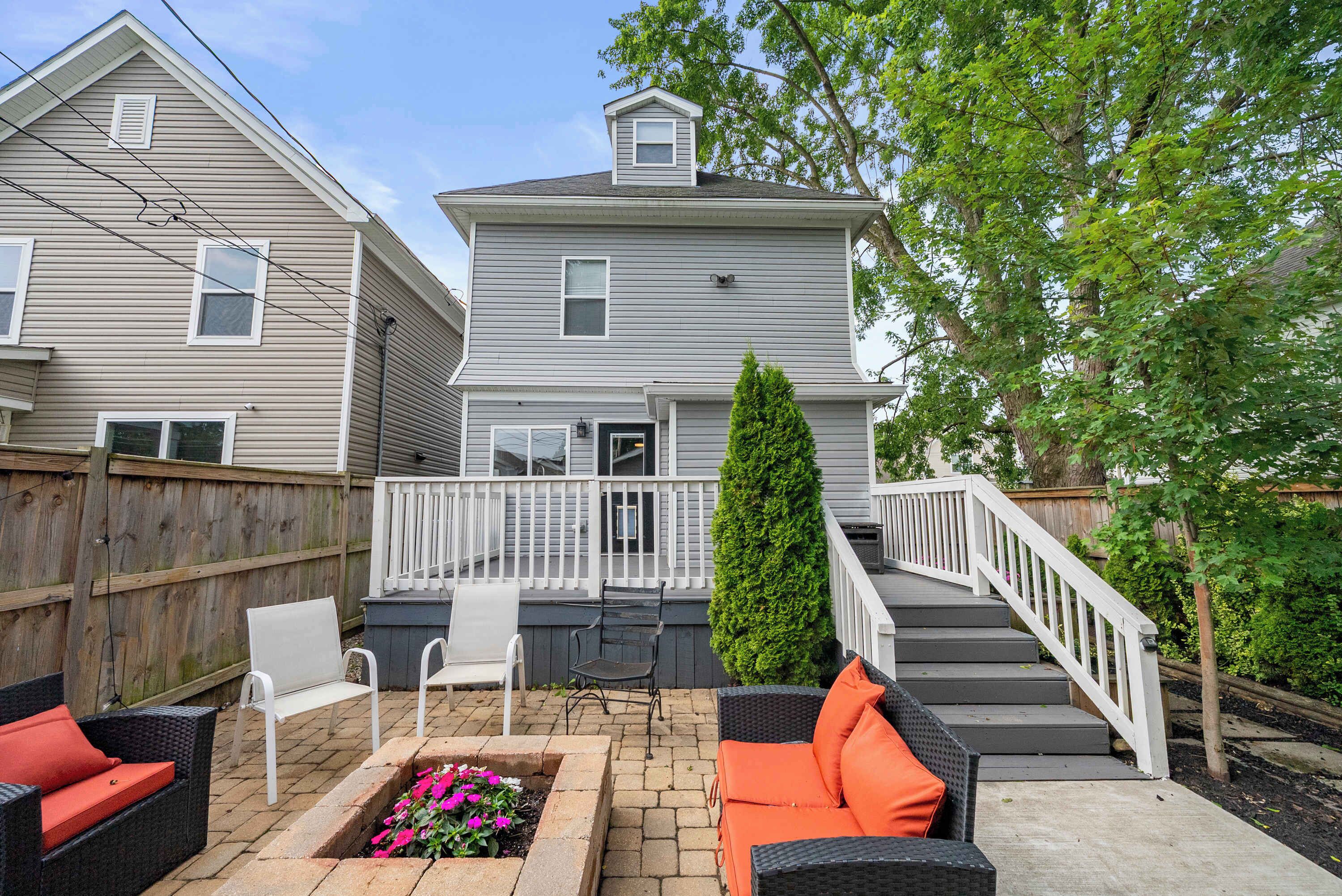 A backyard with a patio area, outdoor furniture, a wooden fence, and a staircase leading to a deck.