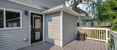 Ein Haus mit einer Holzterrasse, einer schwarzen Tür und einem weißen Geländer.