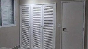 Une chambre à coucher avec un lit, une fenêtre avec des stores et une armoire à portes à persiennes.