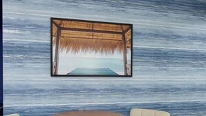 Une pièce avec un mur à texture, un tableau encadré représentant une scène de plage, et deux fauteuils rembourrés disposés autour d’une table ronde en bois.