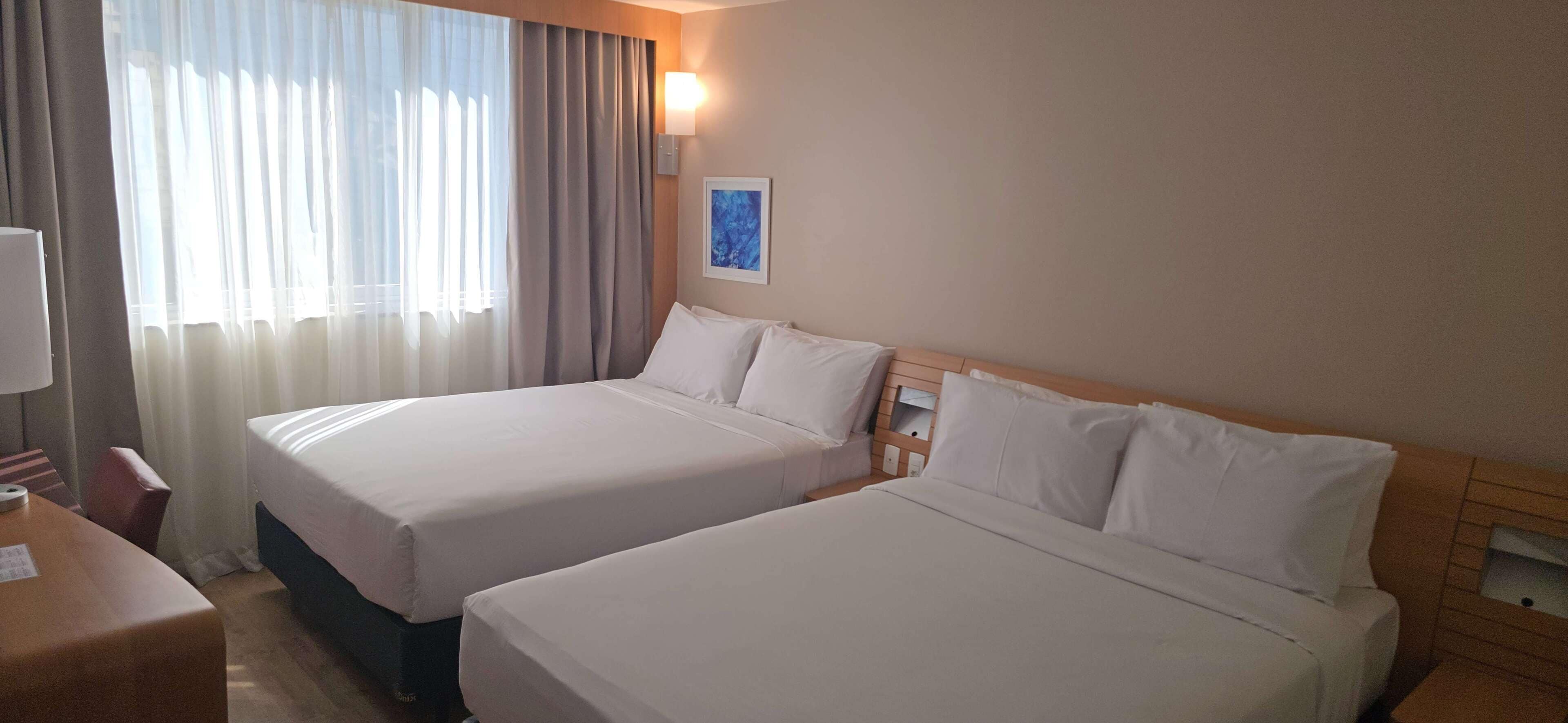 Een hotelkamer met twee bedden, een bureau en een raam met gordijnen.