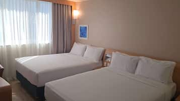 A hotel room with two beds, a desk, and a window with curtains.