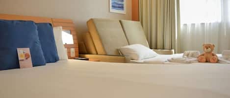 Habitación de hotel con una cama, una silla, un osito de peluche y un cuadro en la pared.