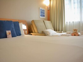 Habitación de hotel con una cama, una silla, un osito de peluche y un cuadro en la pared.