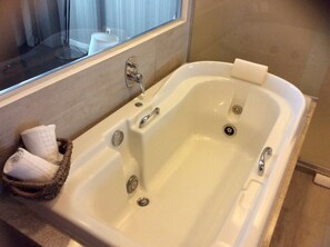 A large, rectangular bathtub with two faucets and a drain, a small basket with towels, and a window above the bathtub. - Regency Barra Hotel (Rio de Janeiro)