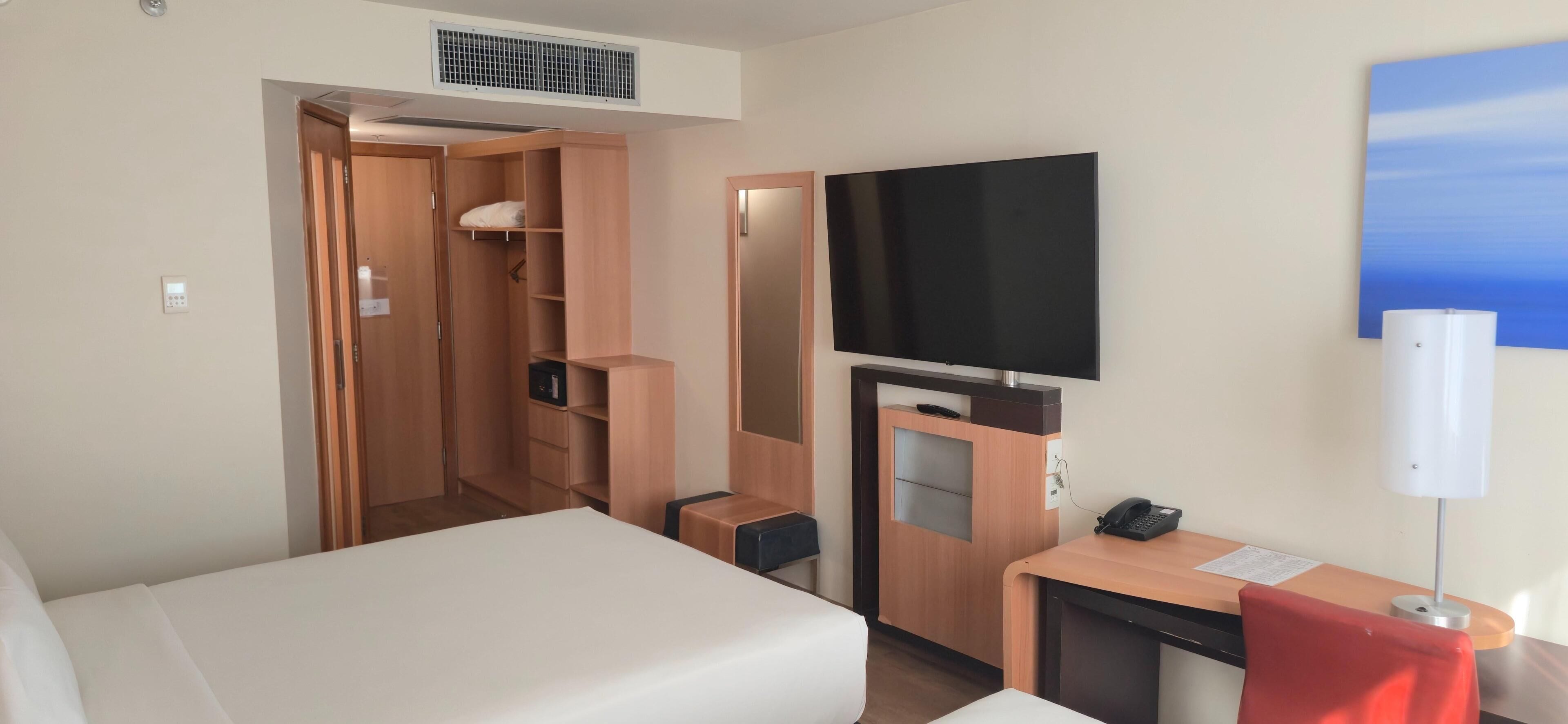 A hotel room with a bed, a desk with a telephone, a television, and a wardrobe.