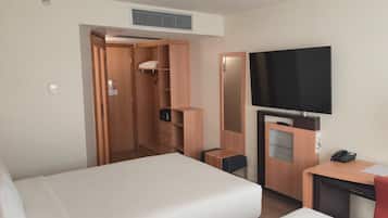 A hotel room with a bed, a desk with a telephone, a television, and a wardrobe.