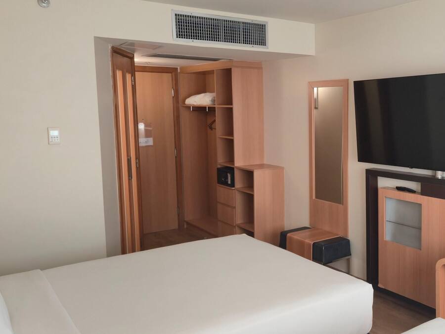 A hotel room with a bed, a desk with a telephone, a television, and a wardrobe.