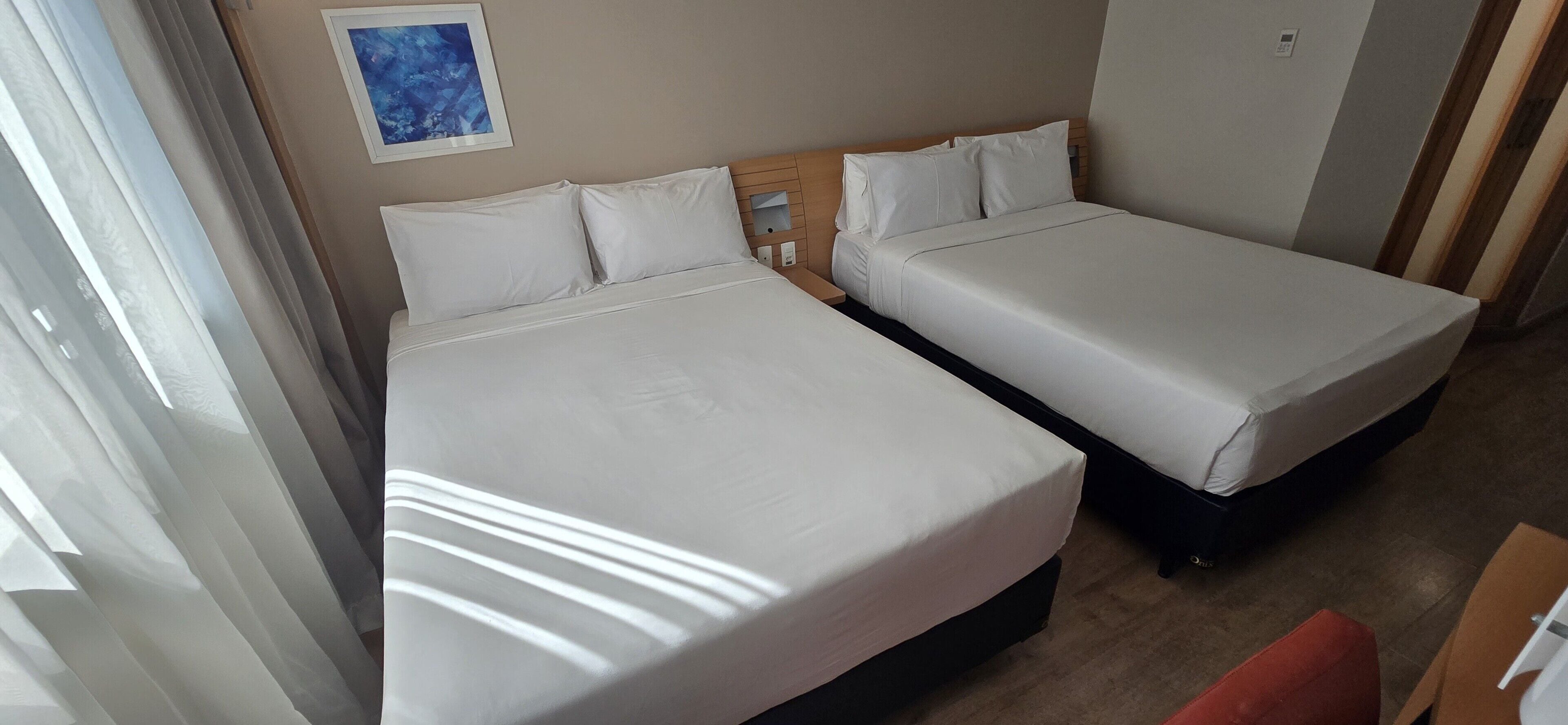 A hotel room with two beds, a wooden headboard, a framed picture on the wall, and a red chair.