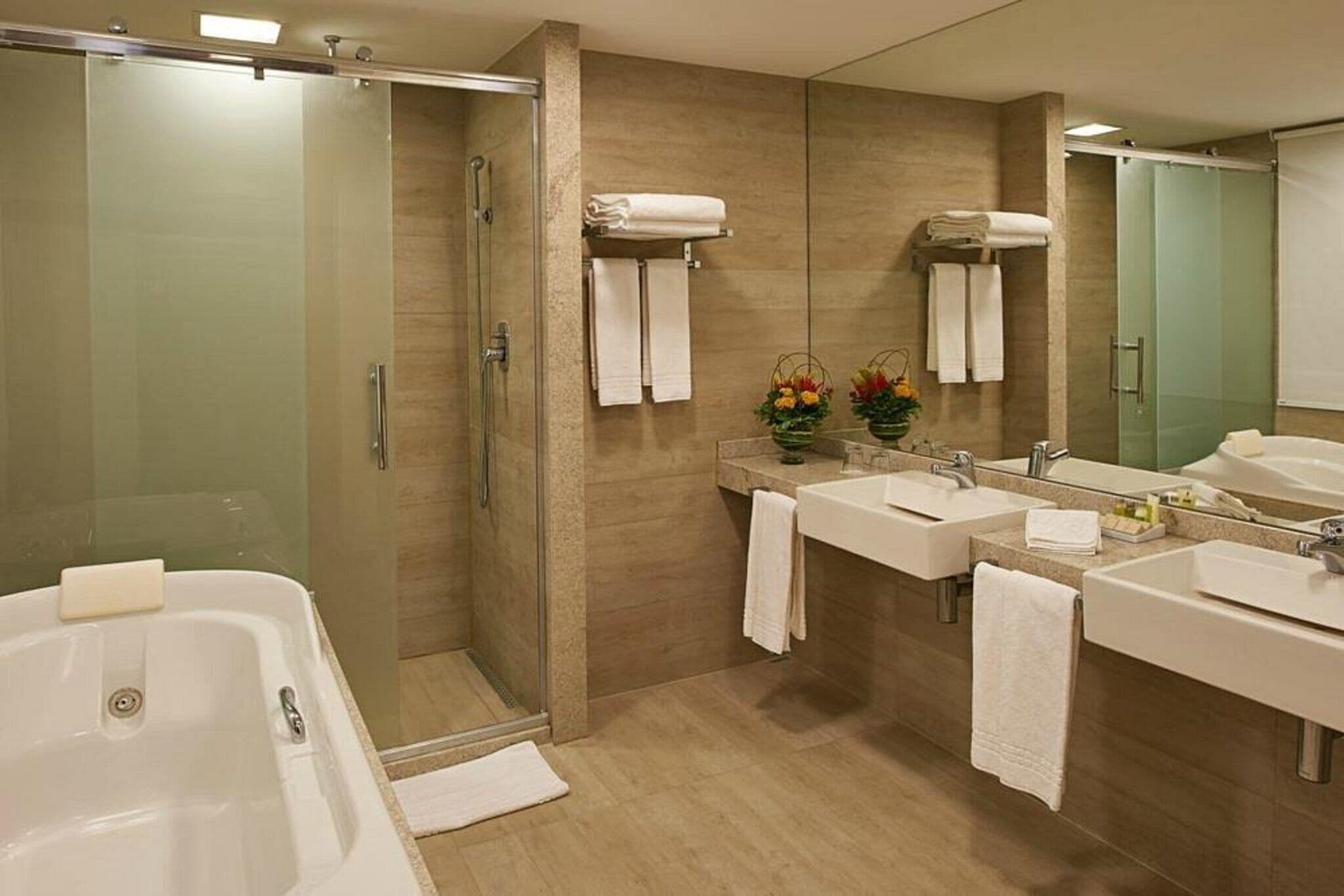 A modern bathroom with a glass-enclosed shower, two sinks, a large mirror, and a bathtub.