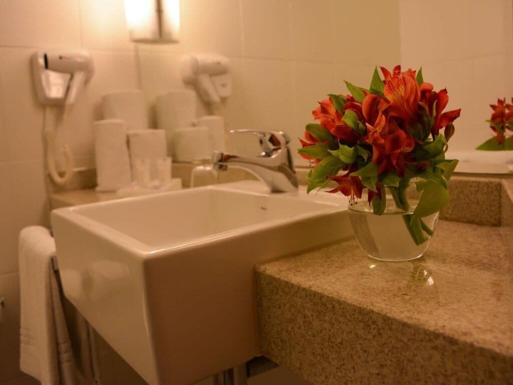 Un baño con lavamanos, espejo, toallero y un florero con flores.
