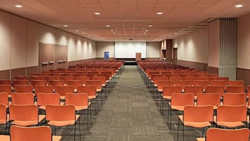Ein Konferenzraum mit Reihen orangener Stühle, einer Projektionsleinwand und einem Rednerpult im Vordergrund.