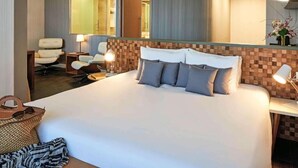 Hotellihuone, jossa on suuri sänky, työpöytä, tuoli ja peili.