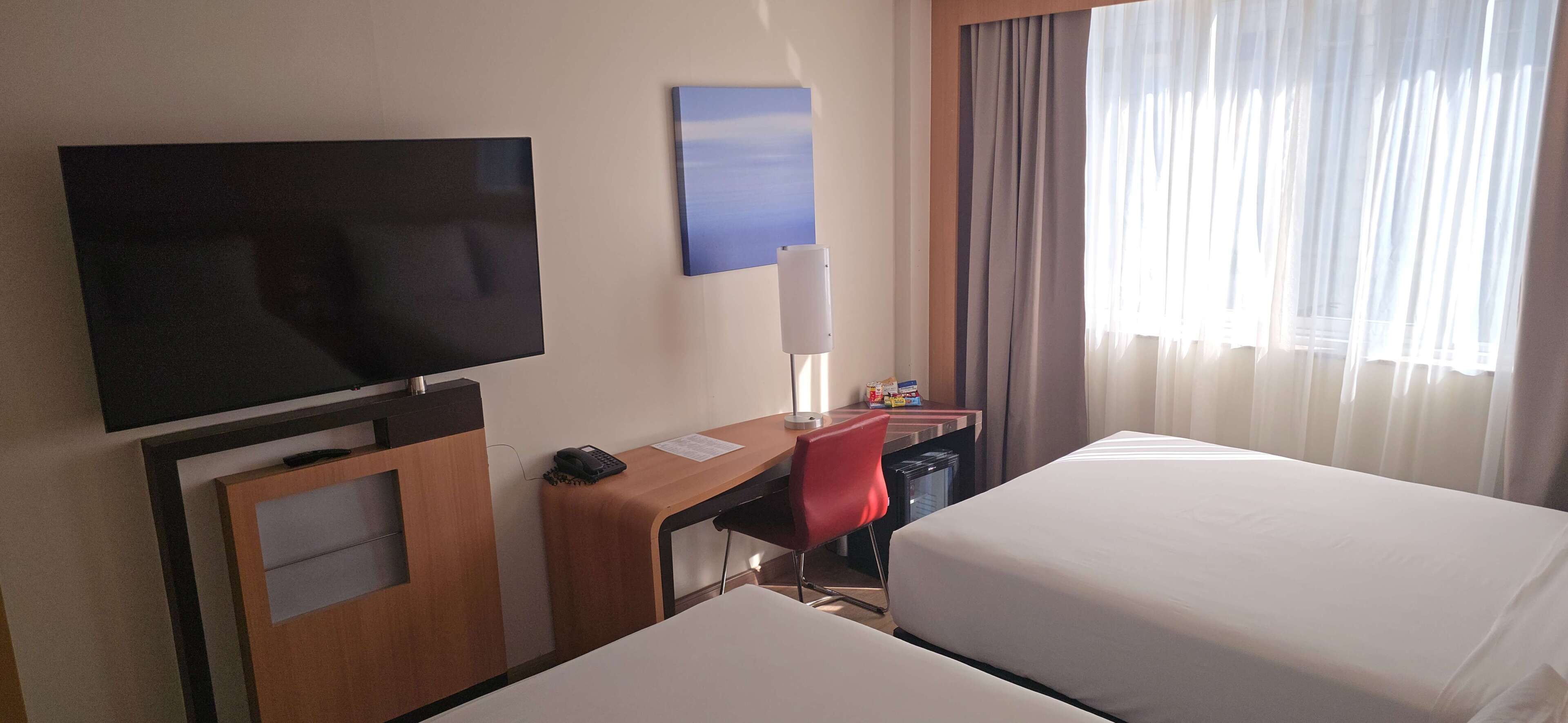Habitación de hotel con televisión, escritorio, silla y dos camas.