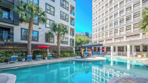 A swimming pool with lounge chairs and umbrellas, surrounded by modern buildings with balconies. - HTX Luxury Downtown Apartments 10 mins away from galleria mall private parking (Houston)
