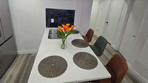 A modern dining area with a white table, four woven placemats, a vase with orange flowers, and two chairs. - The Walkout at the Ravine (Edmonton)