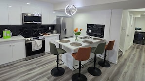 A modern kitchen with white cabinets, a black stove, and a central island with stools. - The Walkout at the Ravine (Edmonton)