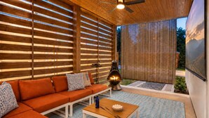A modern outdoor living space with a wooden ceiling, a ceiling fan, a sofa, a table, and a grill.