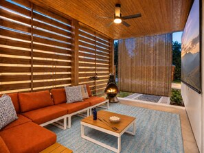 Um espaço ao ar livre moderno com teto de madeira, ventilador de teto, sofá, mesa e churrasqueira.