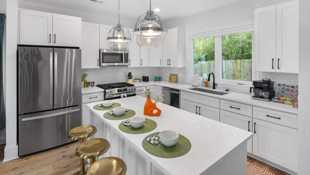 A modern kitchen with white cabinets, stainless steel appliances, a central island with stools, and pendant lighting.