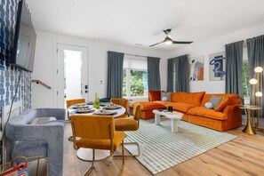 Uma sala de estar moderna com um sofá, cadeiras, uma mesa de jantar e uma TV fixada na parede.