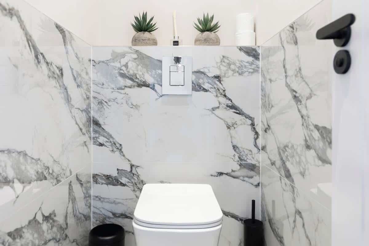 A bathroom with a toilet, marble walls, a hand dryer, and two potted plants.