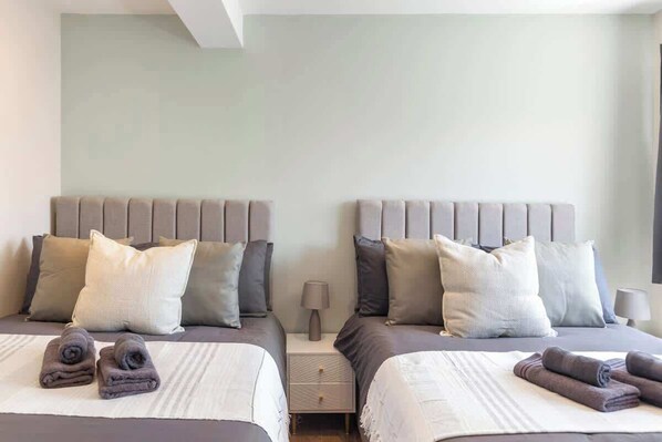 A hotel room with two beds, a nightstand with a lamp, and a window.