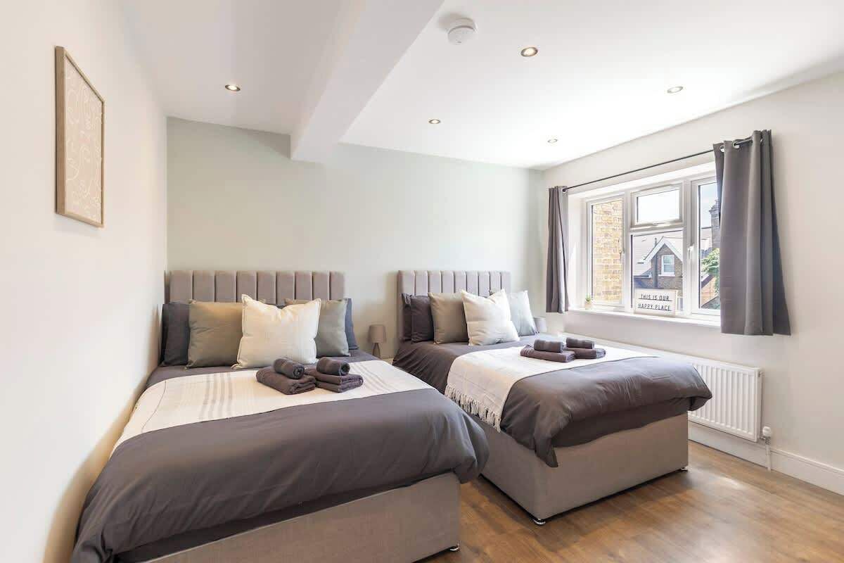 Ein Schlafzimmer mit zwei Betten, einem Fenster mit Vorhängen, einem Heizkörper und einem gerahmten Bild an der Wand.