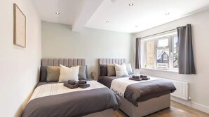 Un dormitorio con dos camas, una ventana con cortinas, un radiador y un cuadro en la pared.