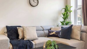 Una sala de estar con sofá, una mesa de centro, un reloj y una planta.