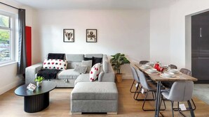 A modern living room with a grey sofa, a dining table set for four, and a ceiling light fixture.