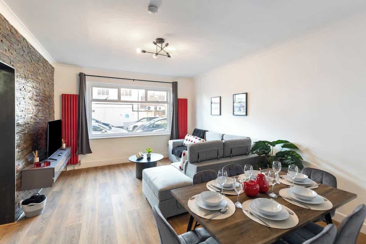 A modern living room with a dining area, a brick accent wall, a large window, and a sofa set.