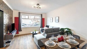 A modern living room with a dining area, a brick accent wall, a large window, and a sofa set. - Spacious House with Private Entrance (London)