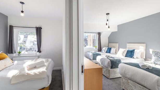 A hotel room with two beds, a window with curtains, a small table, and a mirror.