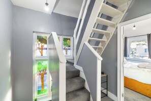 A staircase with a white handrail, grey carpeted steps, and a door leading to a bedroom with a bed.