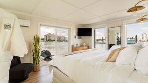 Ein Schlafzimmer mit einem großen Bett, einem Fernseher, einer Pflanze und Blick auf ein Gewässer.