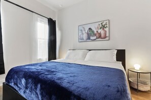 Une chambre à coucher avec un lit, un tableau, une lampe de chevet et une fenêtre avec des rideaux.