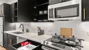 A modern kitchen with black cabinets, a white countertop, a microwave, stove, and a sink.