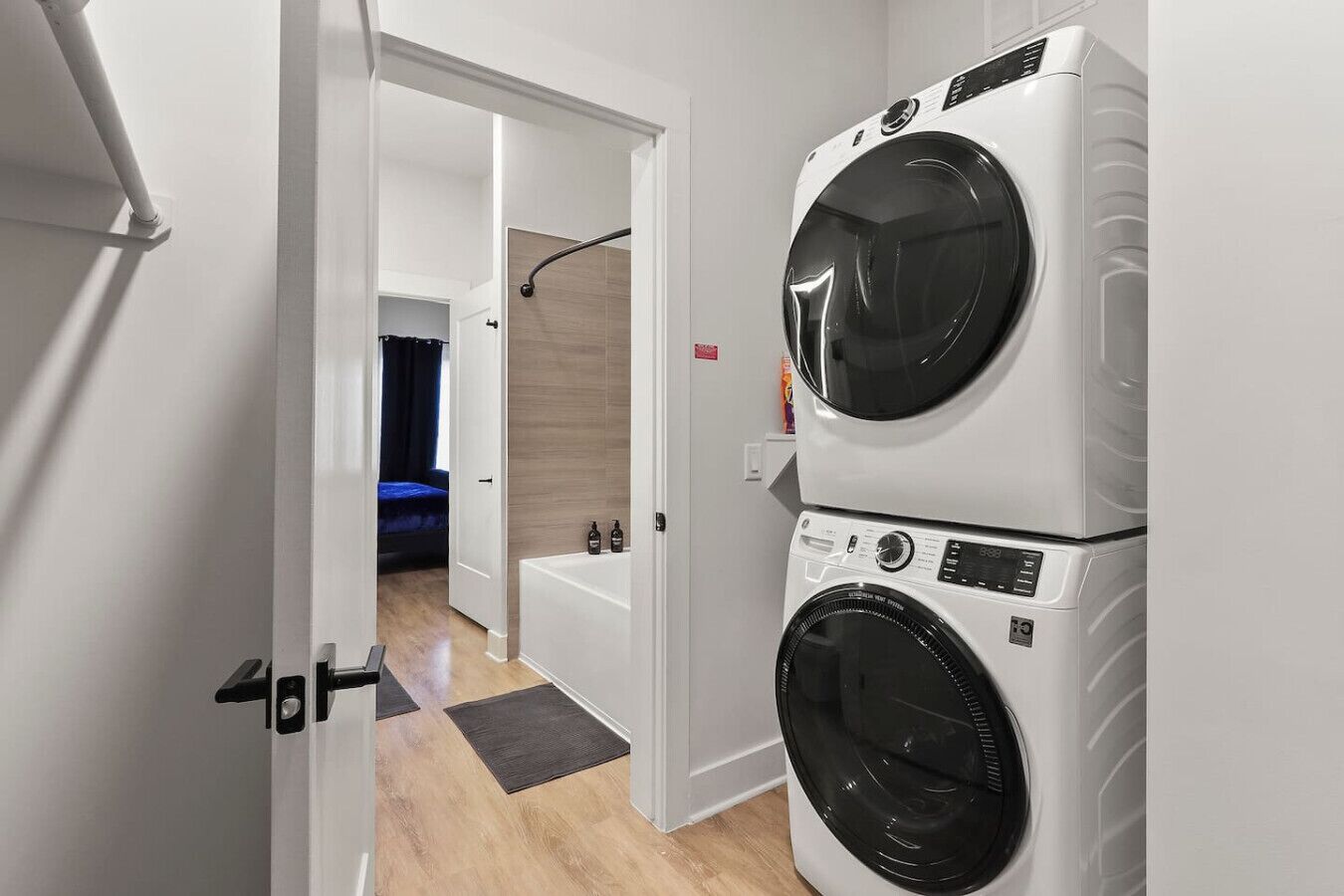 Une buanderie équipée de deux machines à laver superposées et une chambre à coucher visible à travers une porte ouverte.