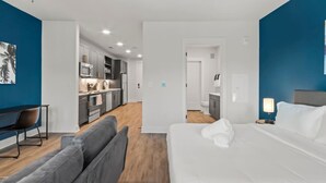 A modern hotel room with a large bed, a sofa, a desk, and a kitchenette. - A+ Relaxing Studio | Walk to Raymond James Stadium (Tampa)