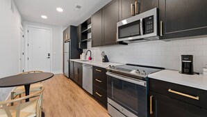 A modern kitchen with dark cabinetry, stainless steel appliances, and a white countertop. - Stylish Studio with One Queen Bed | Raymond James! (Tampa)