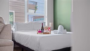 A neatly made bed with white linens, a bedside table with a bottle, a glass, and a pink box. - Stylish Studio with One Queen Bed | Raymond James! (Tampa)