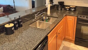 A kitchen with granite countertops, wooden cabinets, a stainless steel sink, a coffee maker, and a dishwasher. - ⛷️Slope side Condo- (Stratton)